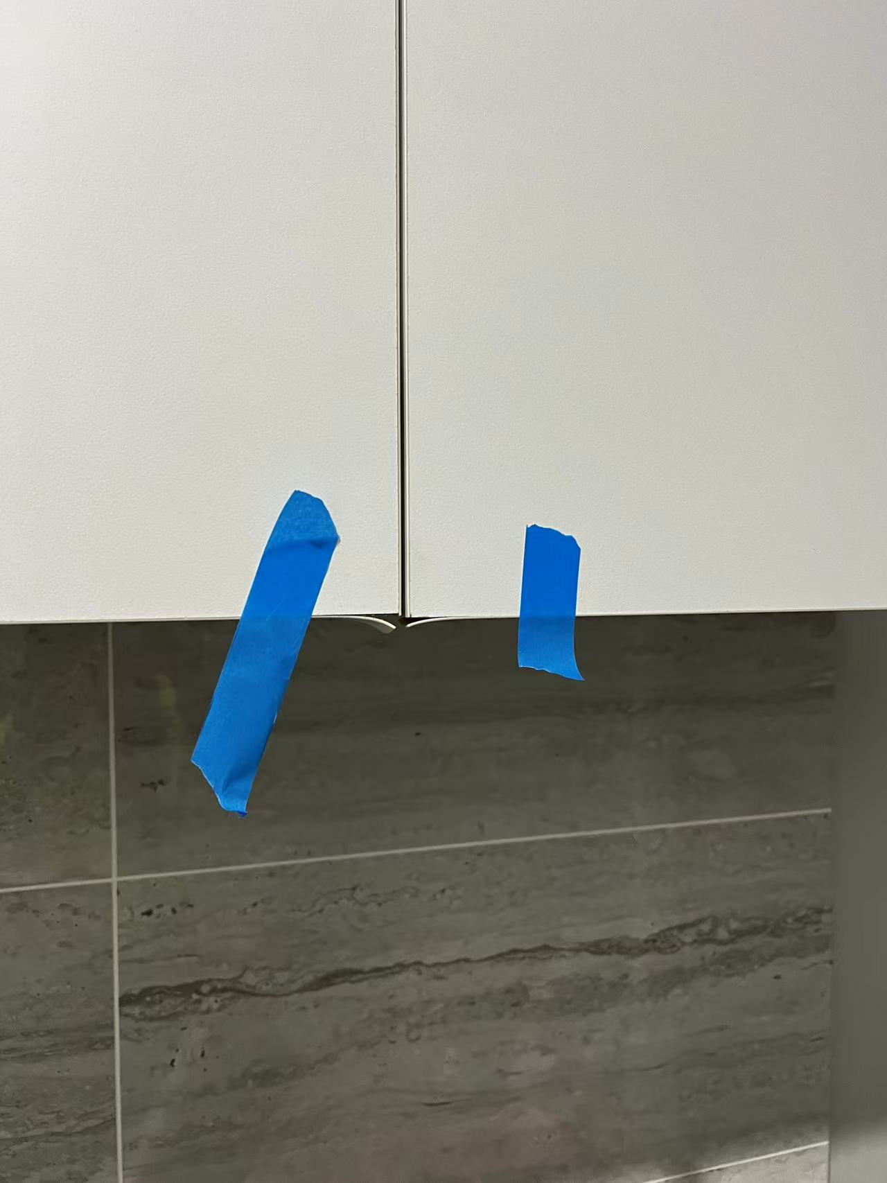 White cupboard doors with blue tape beside lifted lower edges